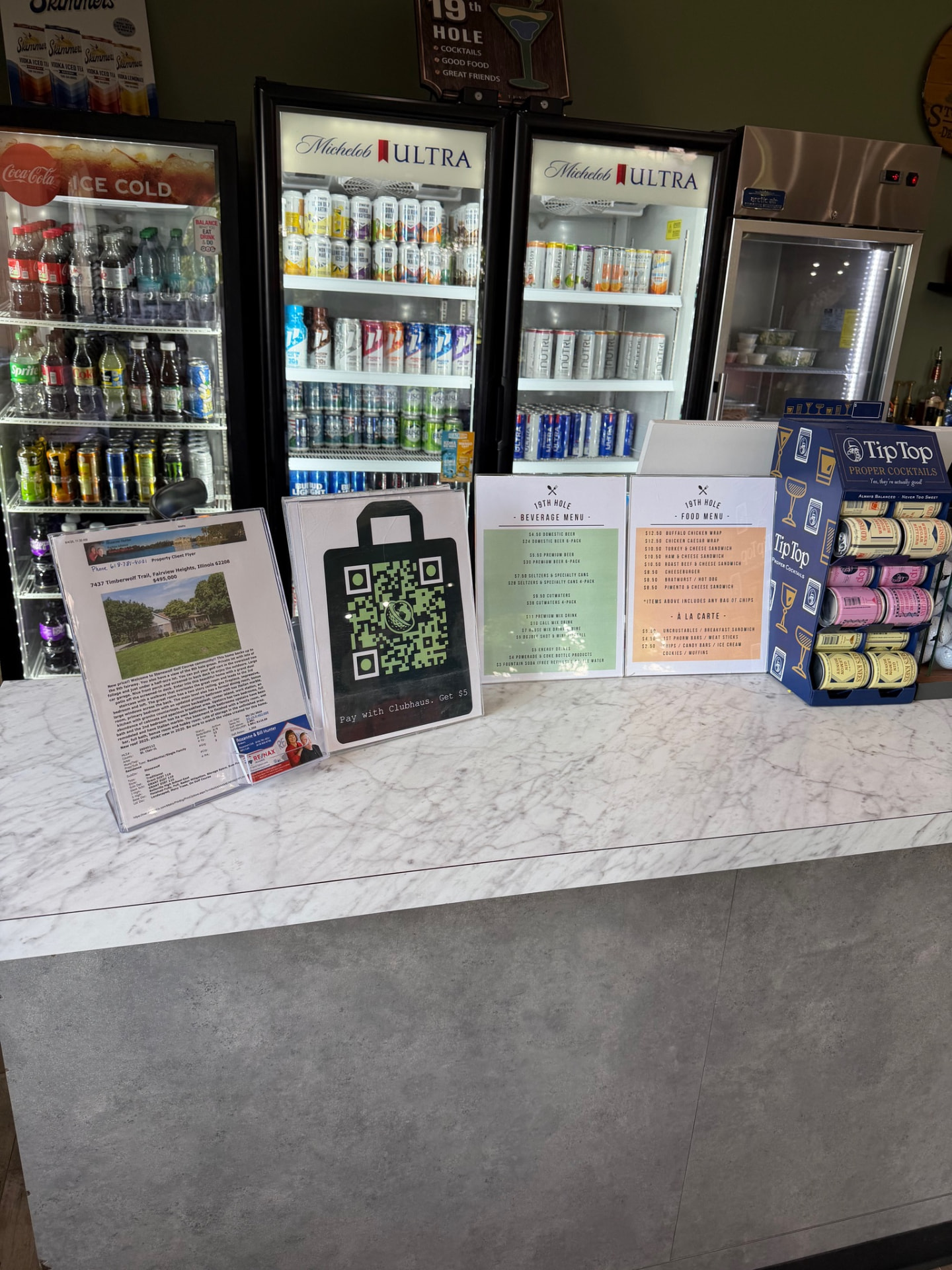 Clubhaus QR display stand on a snack bar counter beside drink coolers and menus